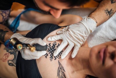 male-tattoo-artist-tattooing-young-woman-in-tattoo-studio-400-222895164.jpg
