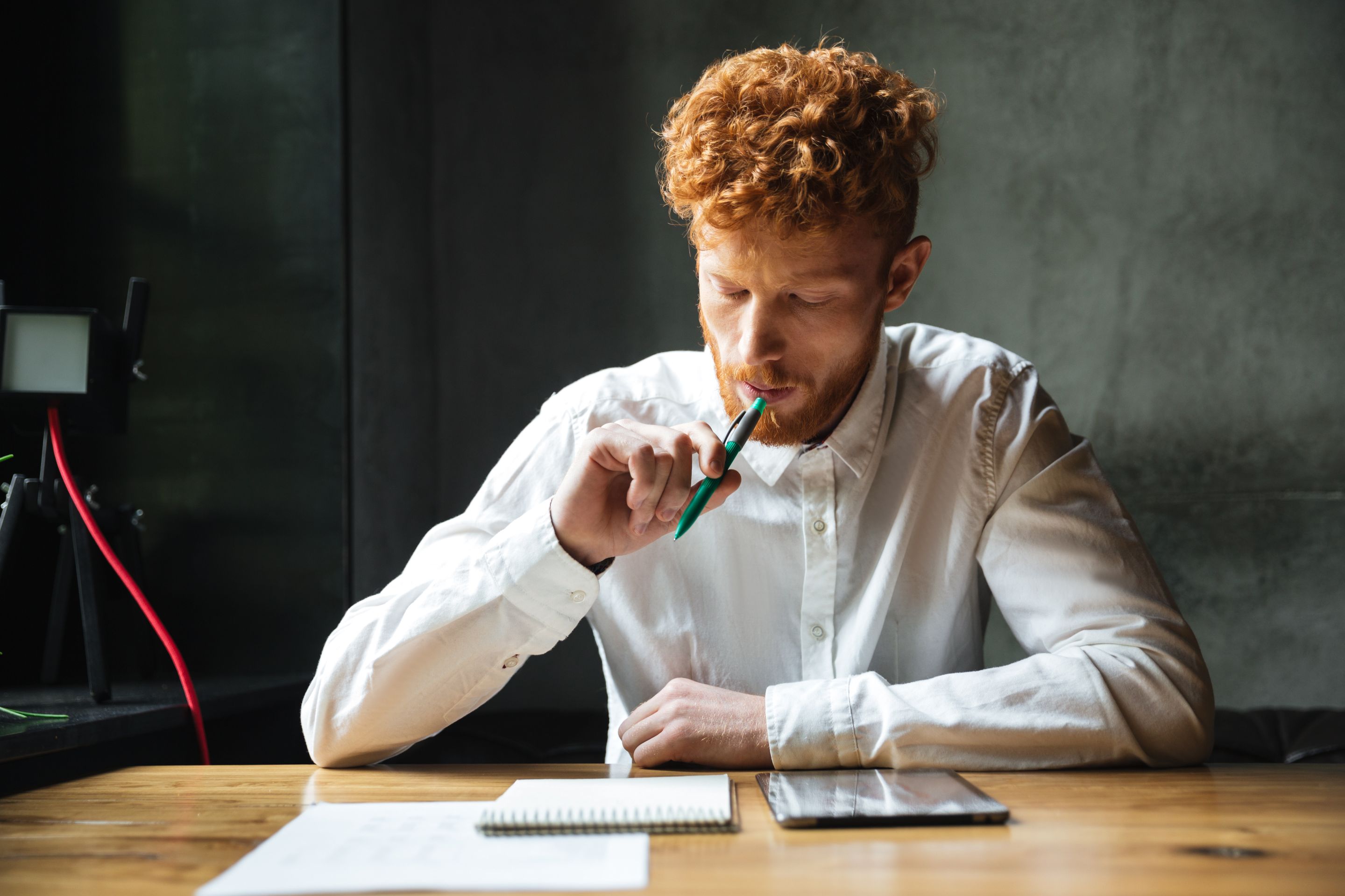 portrait-thinking-young-readhead-man-white-shirt-sitting-wooden-table-with-pen-his-mouth.jpg
