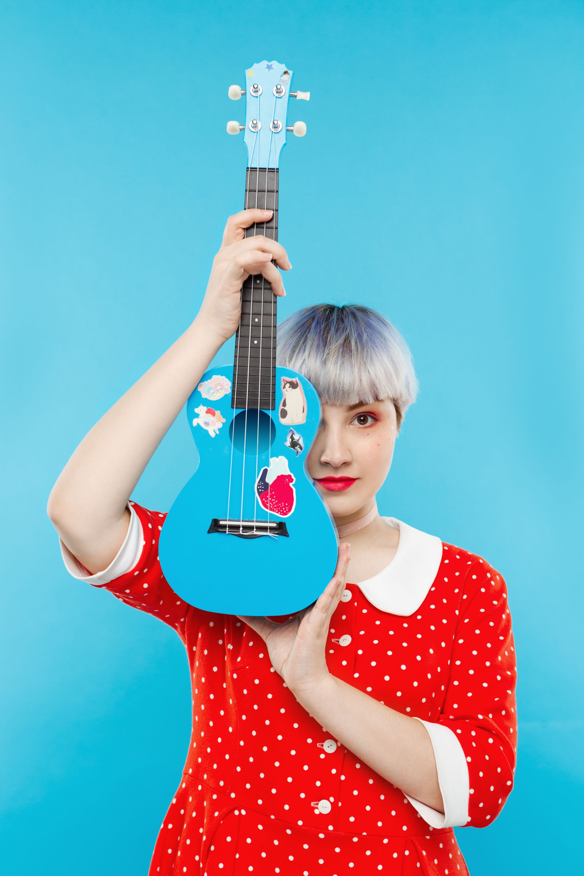 0000cierrese-encima-del-retrato-de-la-muchacha-dollish-hermosa-con-el-pelo-violeta-claro-corto-que-lleva-el-vestido-rojo-que-sostiene-el-ukelele-sobre-la-pared-azul.jpg