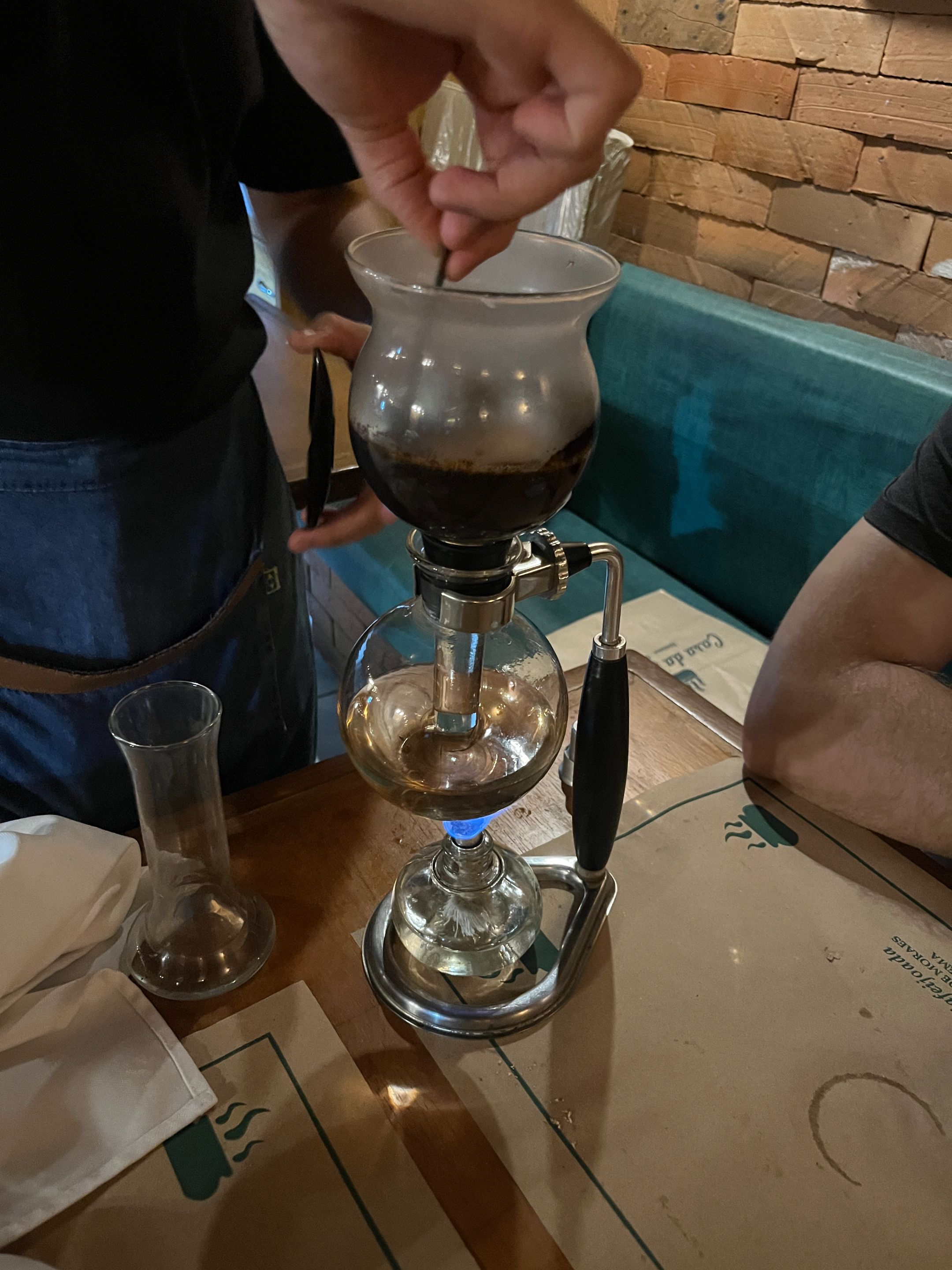 the waiter opens the top chamber and stirs the grounds